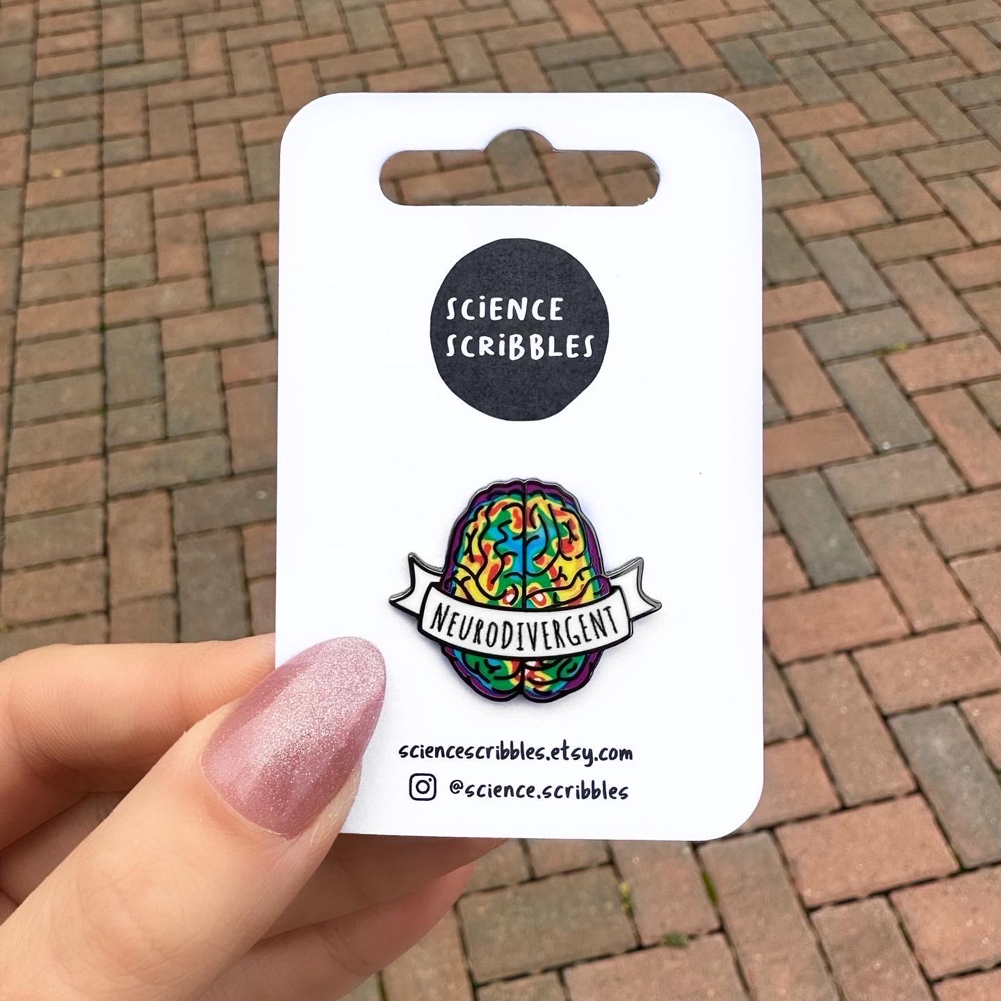Pin with 'Neurodivergent' design on a 'Science Scribbles' card held by a hand against a brick background.