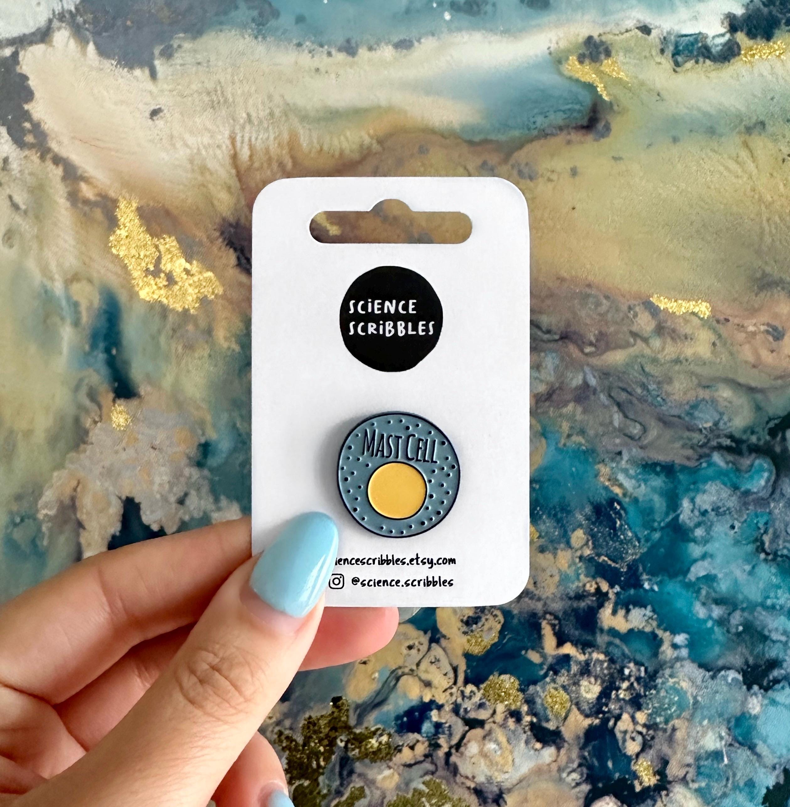 Pin with 'Mast Cell' design on a 'Science Scribbles' card held against a textured background.