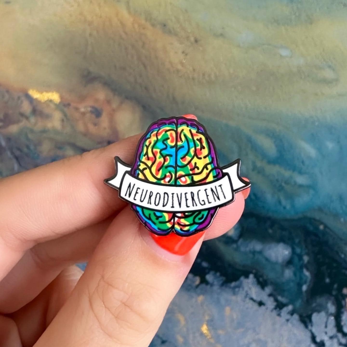 Colorful brain pin with 'Neurodivergent' text held by a hand against a natural background.