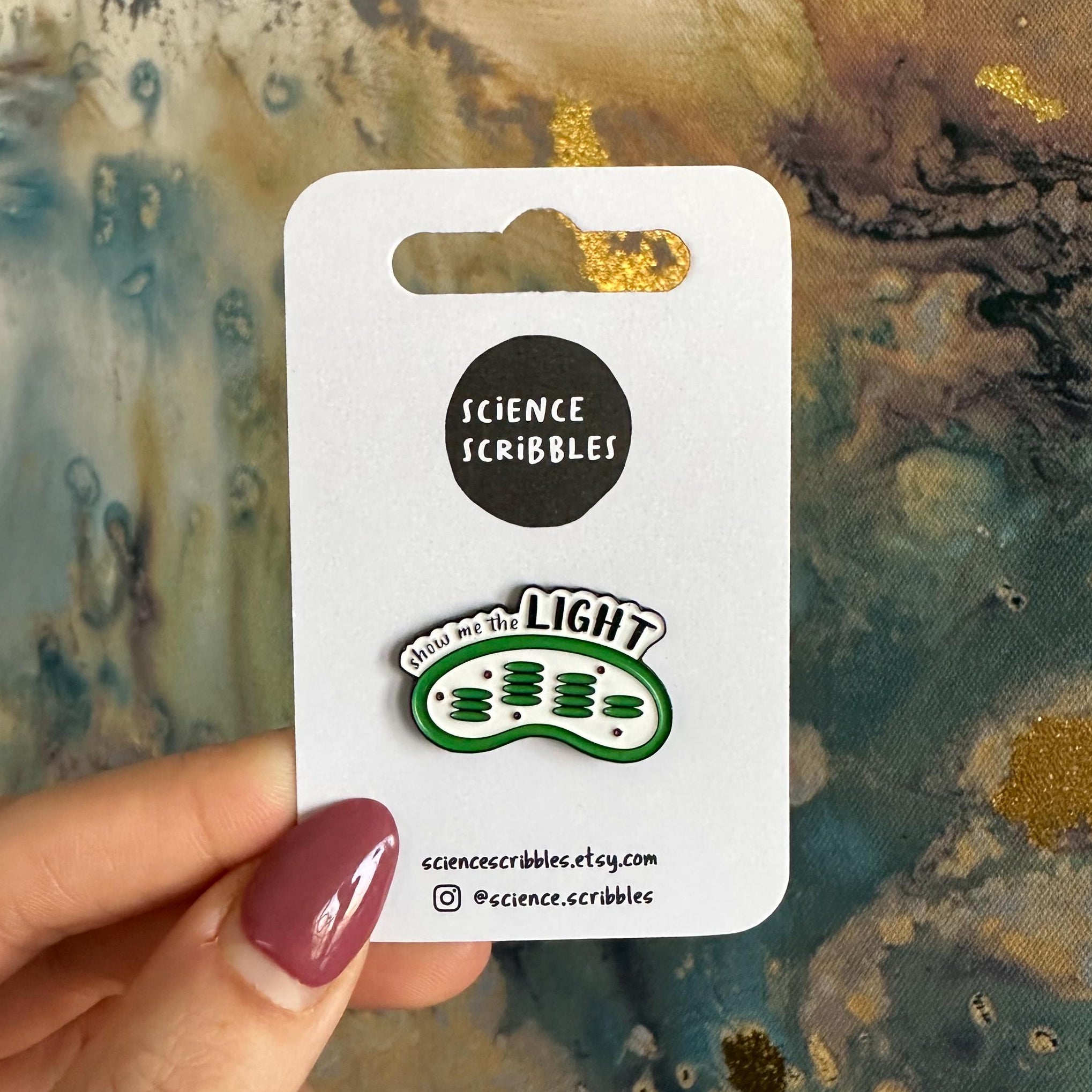 Chloroplast enamel pin on a card held by a hand with a textured background
