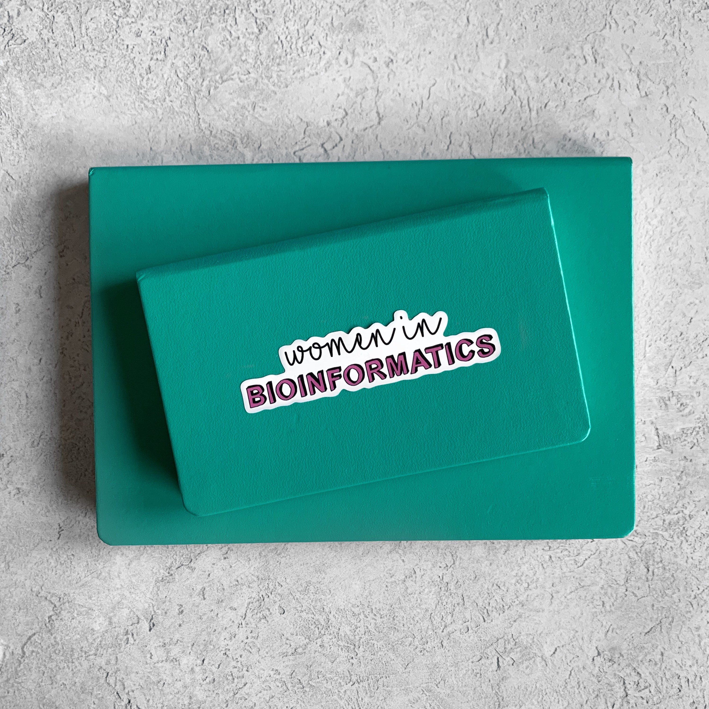 Teal box with 'women in BIOINFORMATICS' sticker on a gray textured background