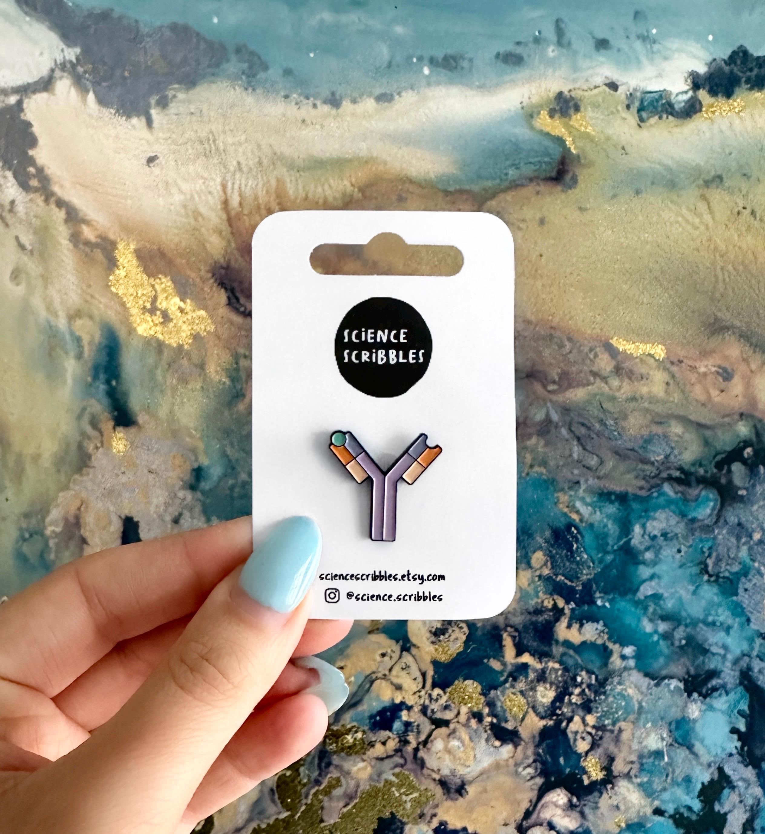Antibody purple and orange enamel pin badge against a colourful background