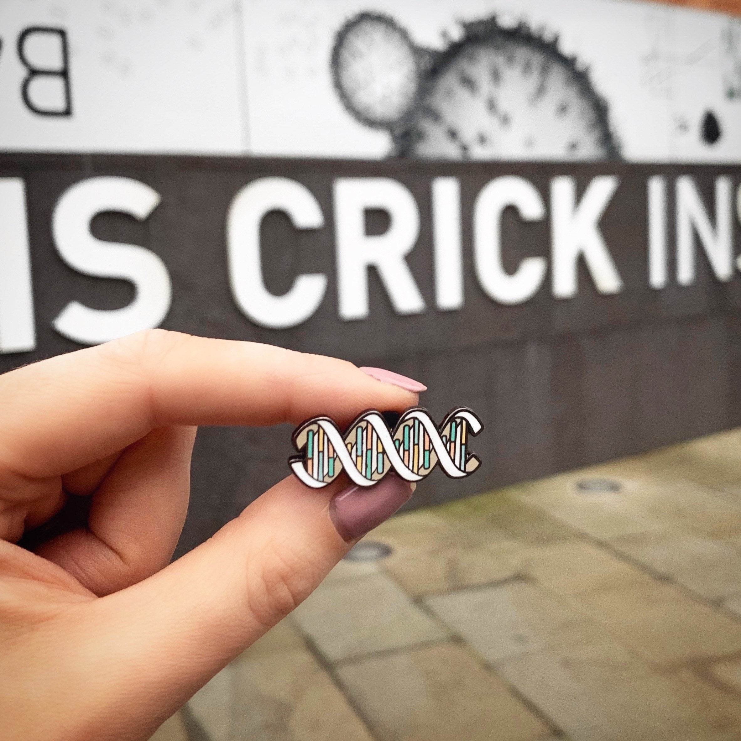 Hand holding a DNA pin outside the Francis Crick Institute in London.