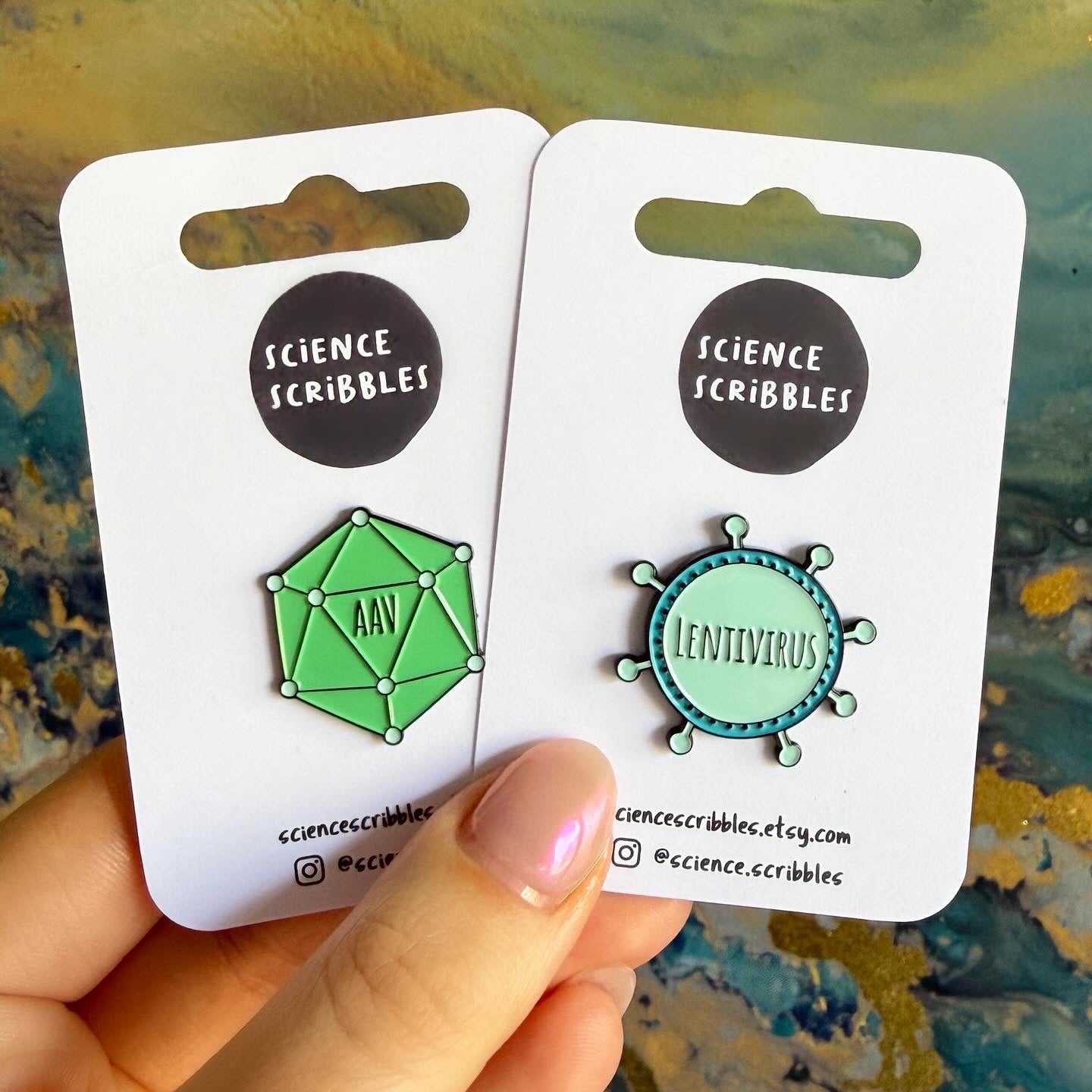 Two green pins on 'Science Scribbles' cards held by a hand against a textured background.