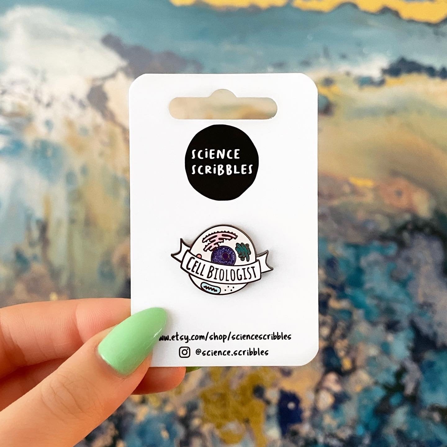 Pin with 'Science Scribbles' branding held by a hand against a colorful abstract background