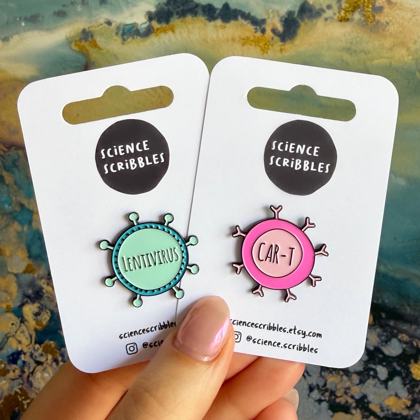 Two science-themed pins on cards held by a hand with a textured background