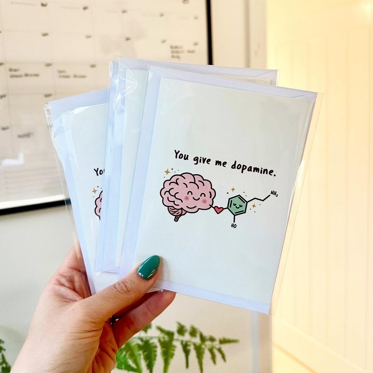Hand holding three small cards with brain and chemical graphics, text 'You give me dopamine', against a blurred indoor background.