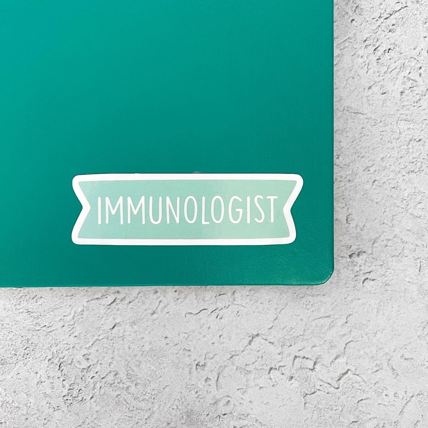 Sticker with 'IMMUNOLOGIST' text on a teal notebook