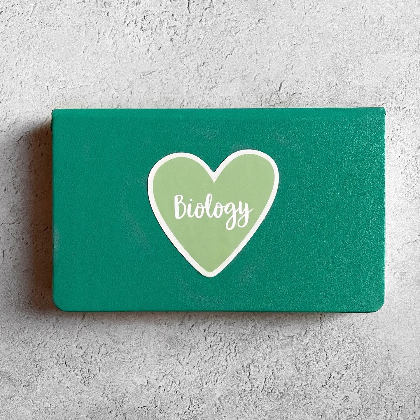Green book with a heart-shaped logo and 'Biology' text on a gray background