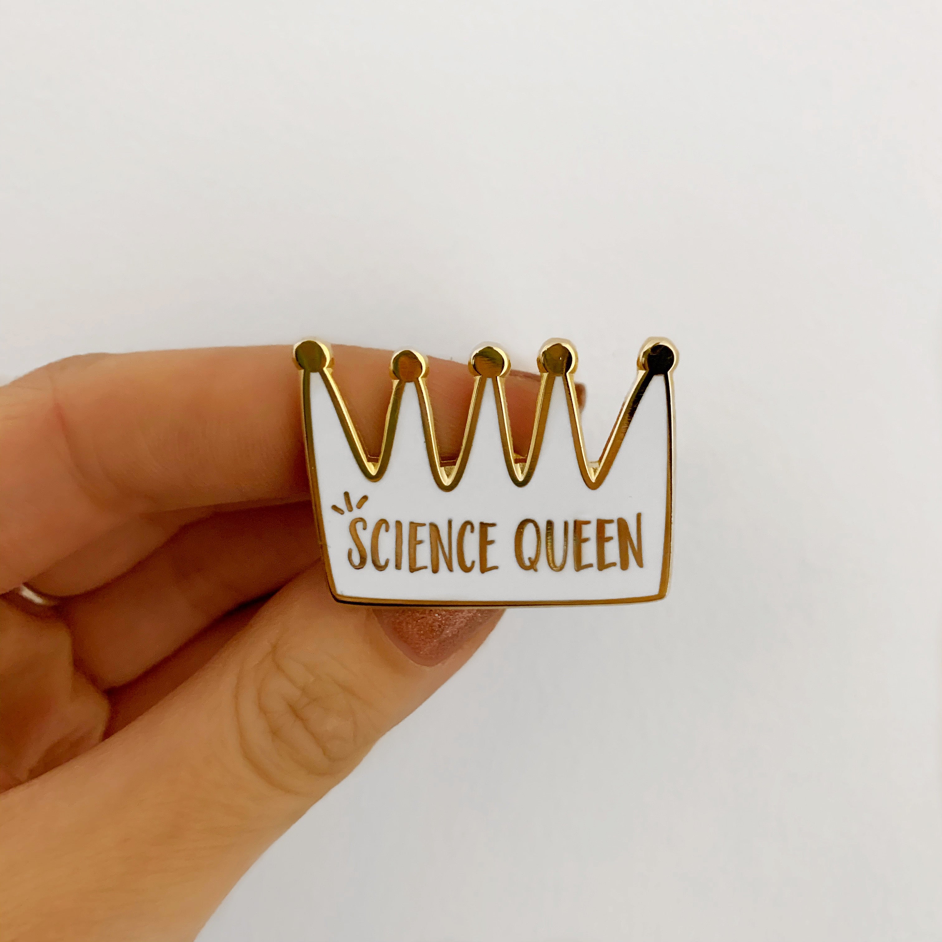 Pin with 'Science Queen' text held by a hand on a white background