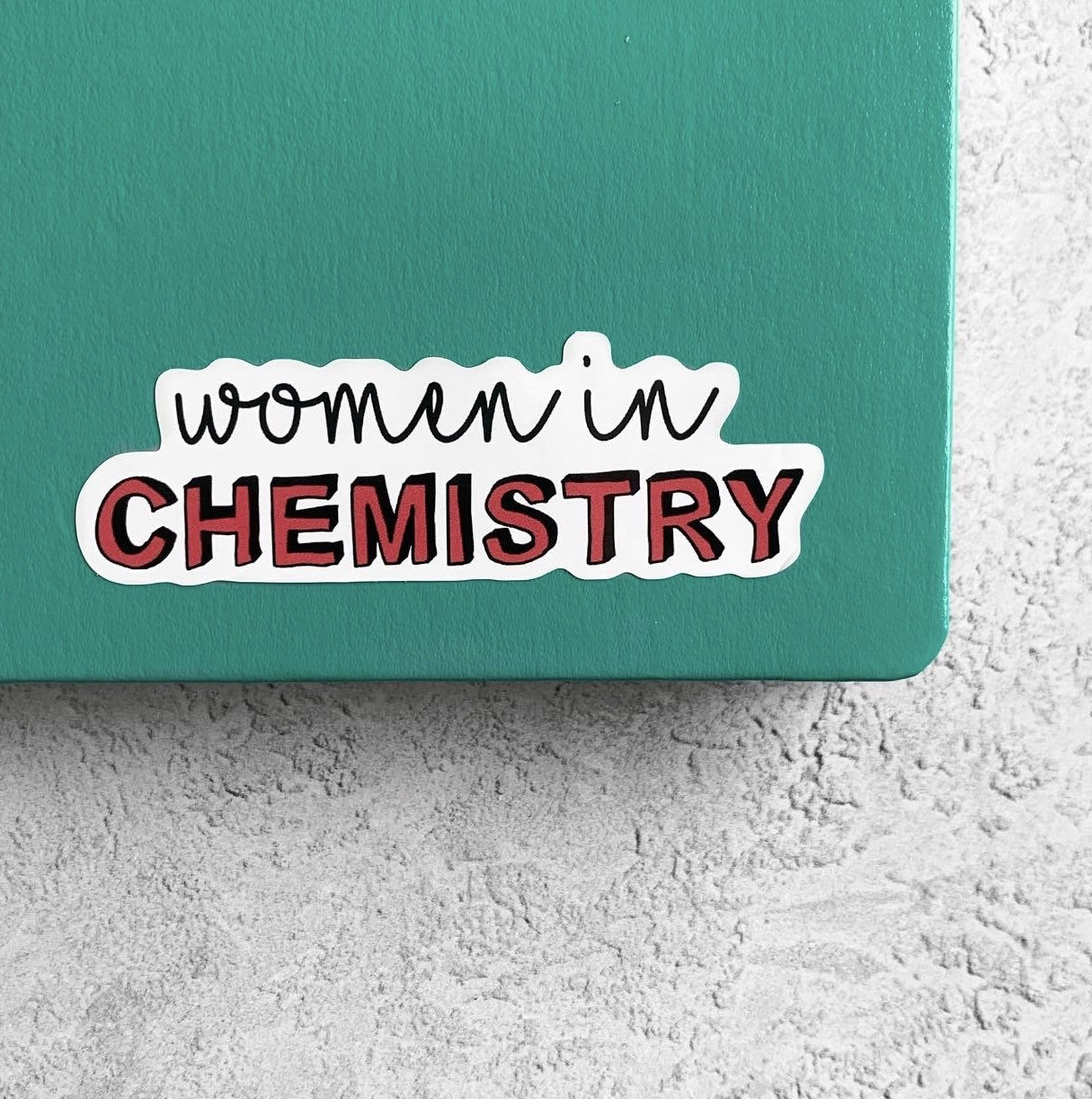 Sticker with 'women in CHEMISTRY' text on a green notebook