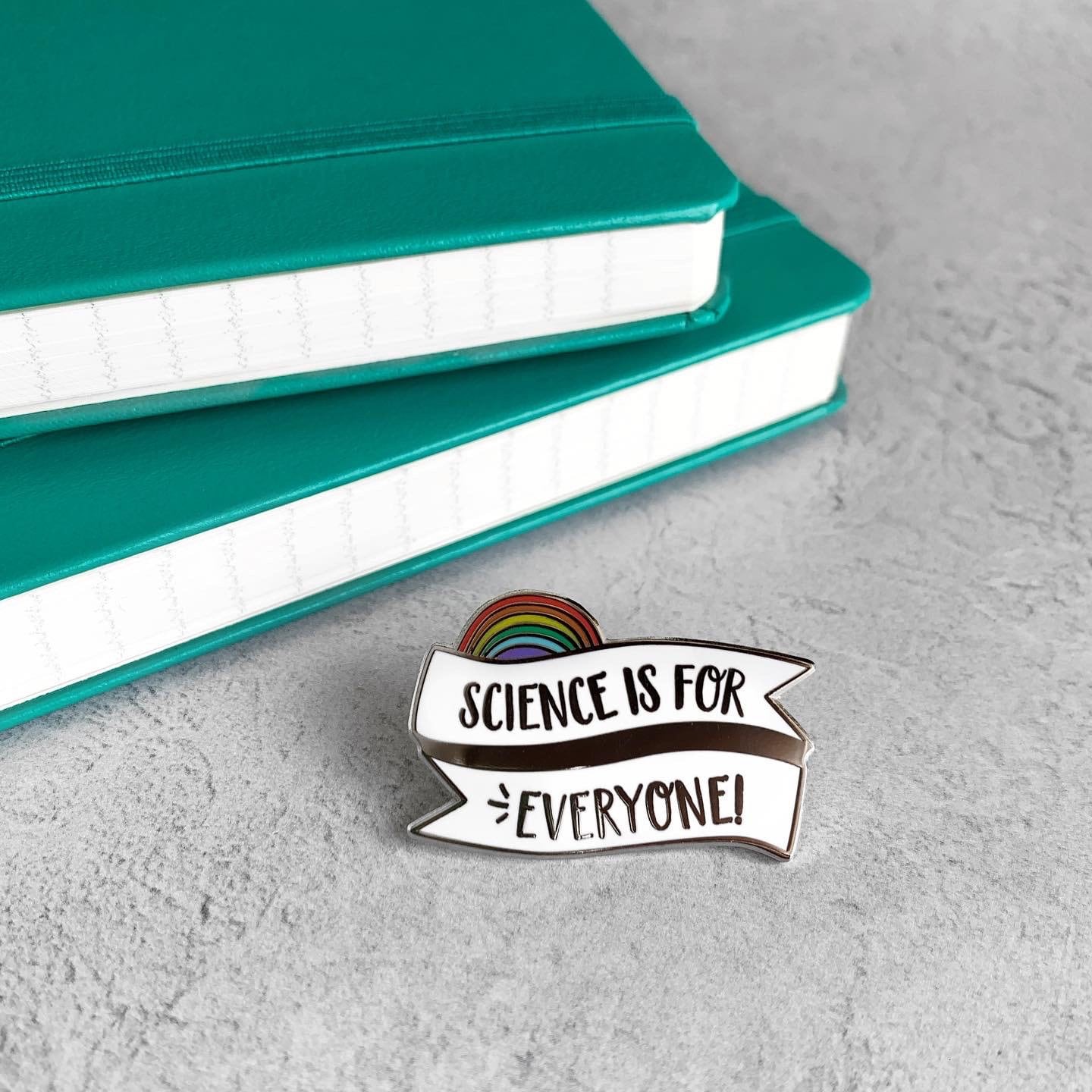 Pin with 'Science is for Everyone!' text on a gray surface with teal books in the background