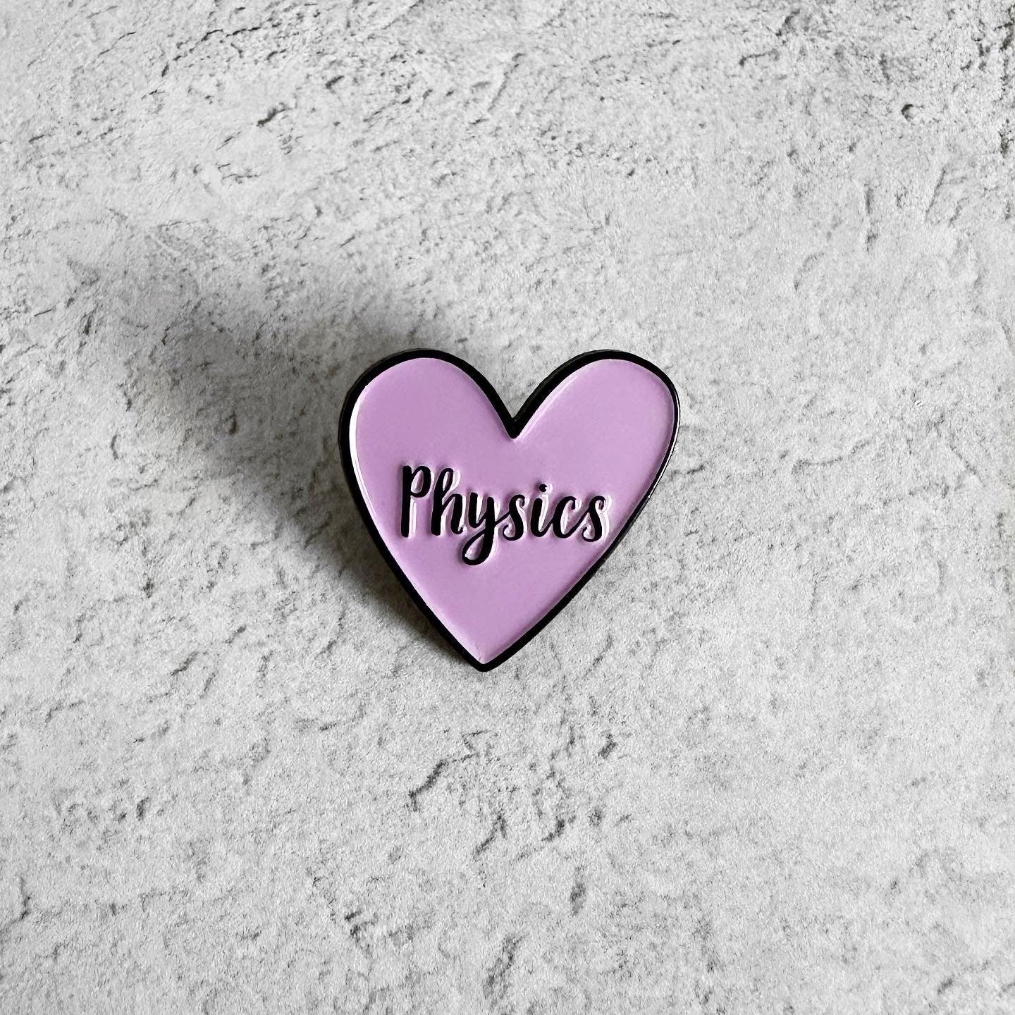 Heart-shaped pin with 'Physics' text on a textured gray background
