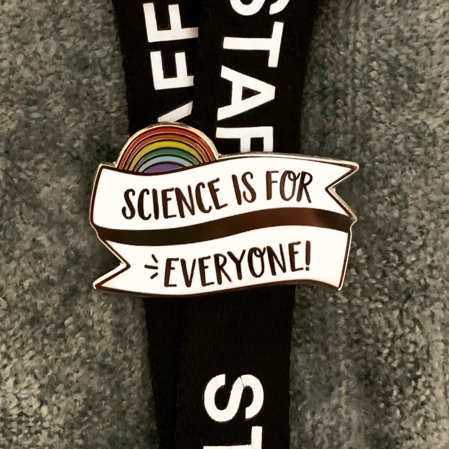 Pin with 'Science is for Everyone!' banner and rainbow design on a black lanyard
