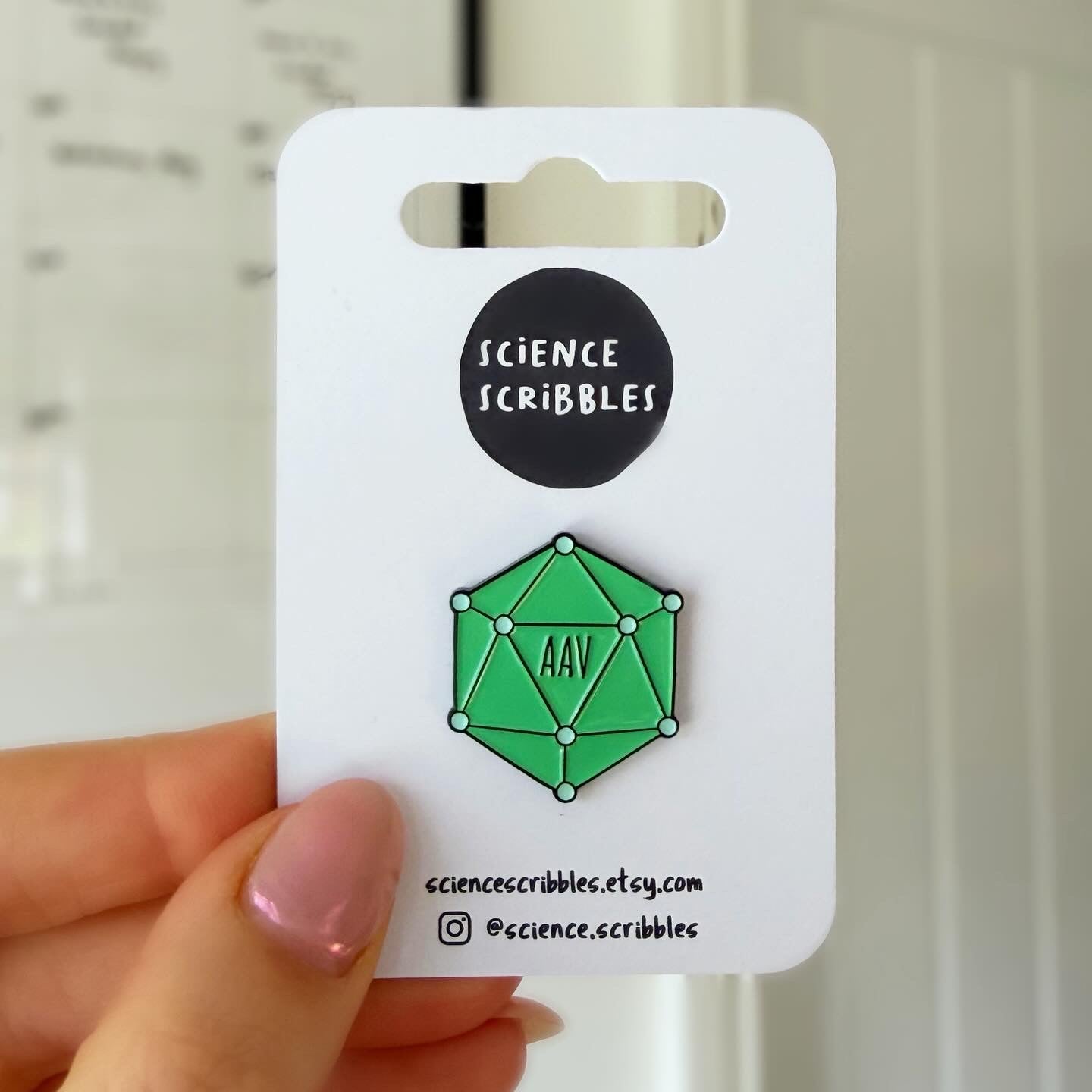 Green geometric pin on a 'Science Scribbles' card held by a hand.
