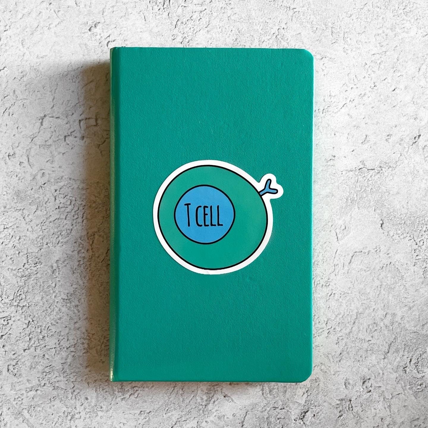 Green notebook with a 'T Cell' illustration on a textured gray surface