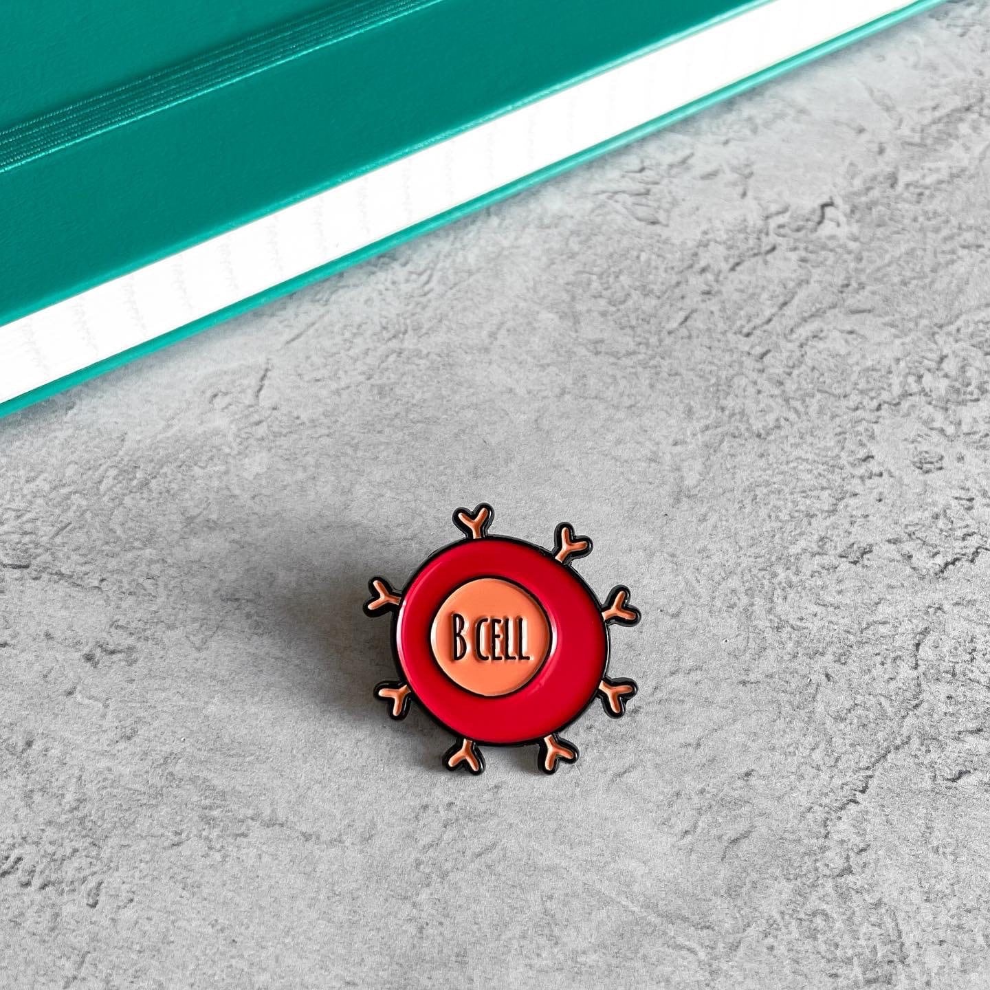 Pin with 'B CELL' design on a textured surface