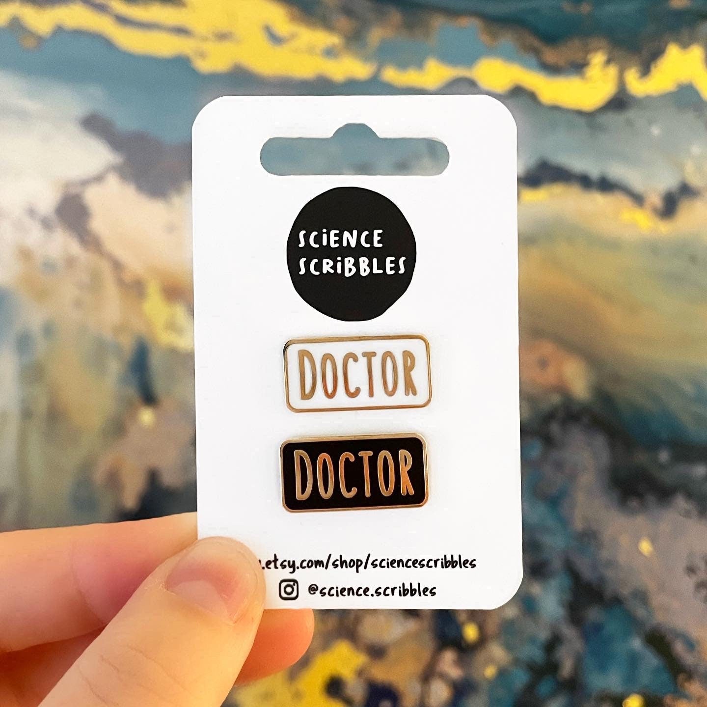 Card with 'Science Scribbles' branding and two 'DOCTOR' pins held against a blurred painting background.