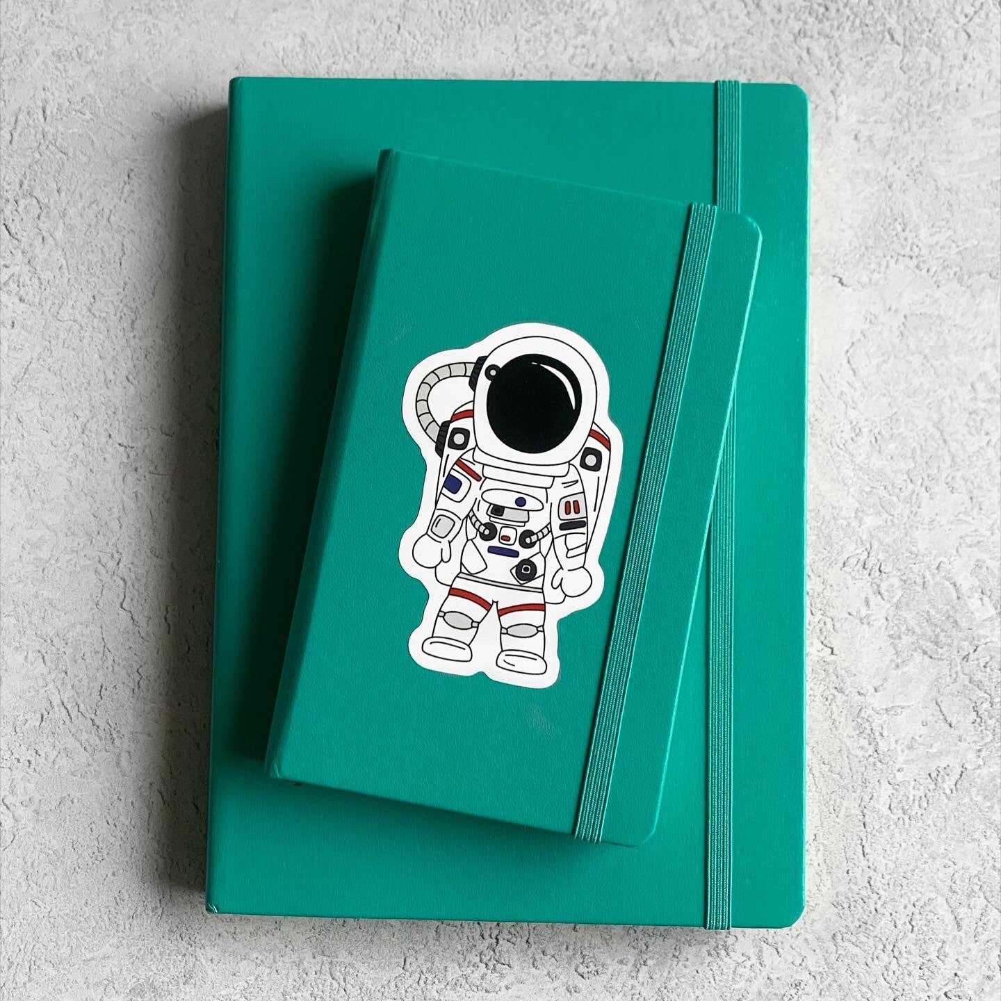 Teal notebook with an astronaut sticker on a light gray background