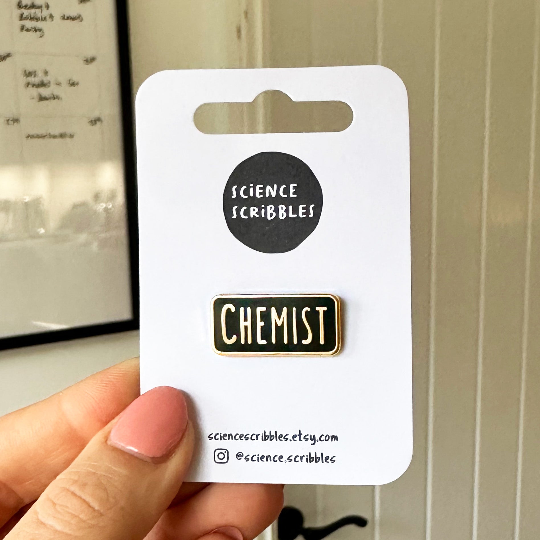 Pin with 'CHEMIST' text on a card labeled 'Science Scribbles' held by a hand.