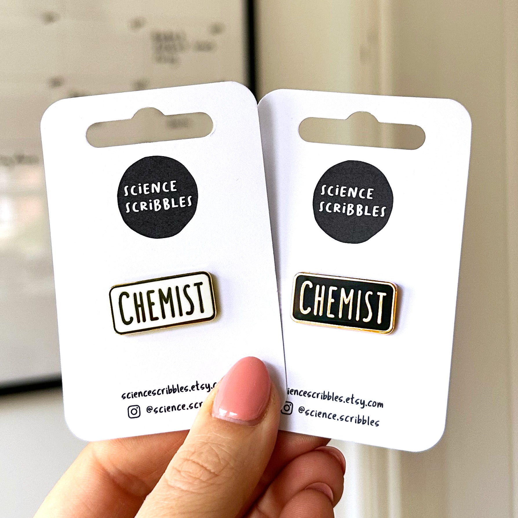 Two 'CHEMIST' pins on cards held by a hand with a blurred background