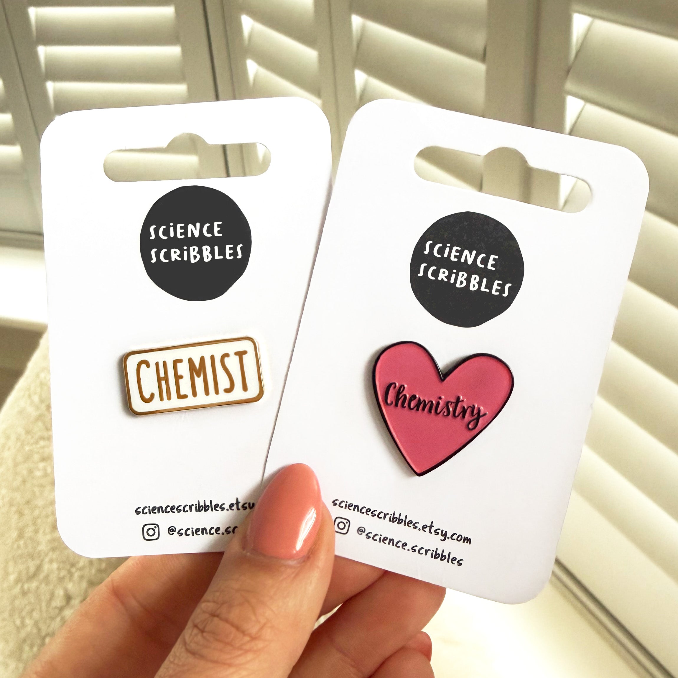 Two pins on cards labeled 'Science Scribbles' held by a hand.