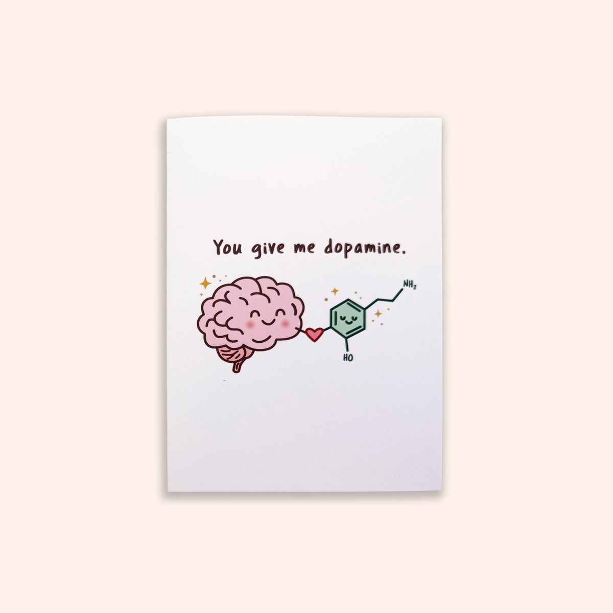 A white rectangular card or print centered on a pale beige background, featuring a cartoon pink brain next to a green dopamine molecule and the text 'You give me dopamine.'.