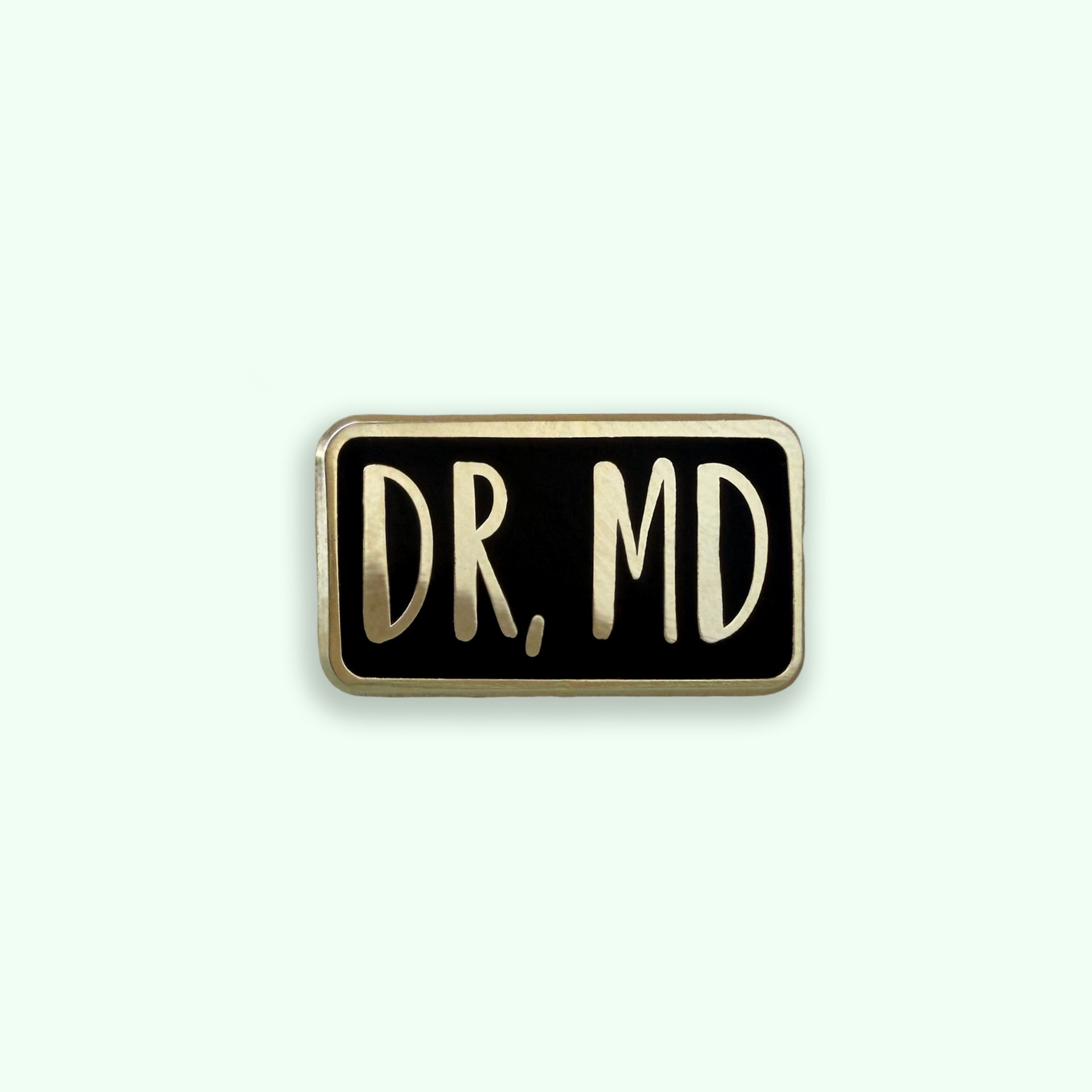 Dr MD black and gold enamel pin badge on green background