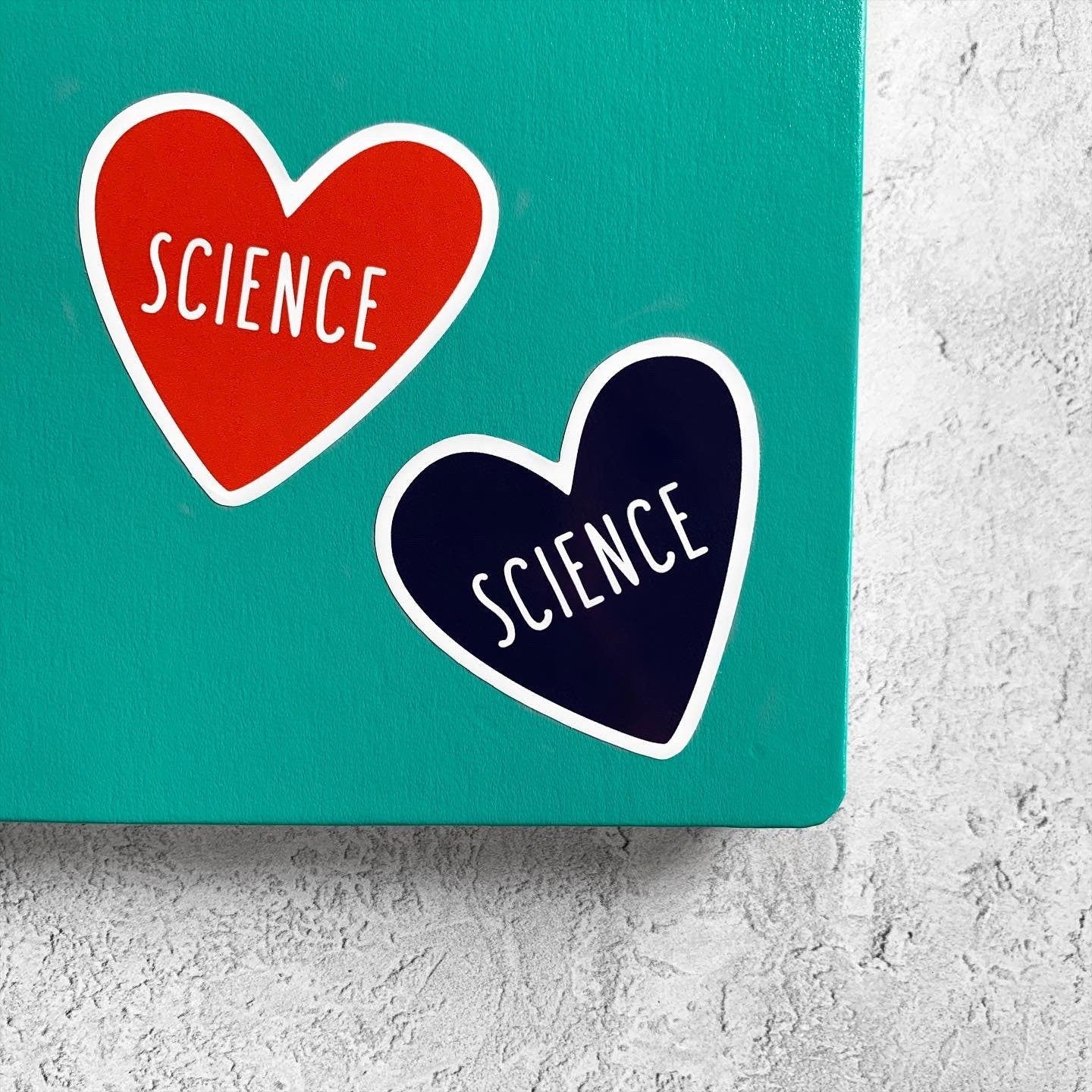 Two heart-shaped stickers with 'SCIENCE' text on a teal background