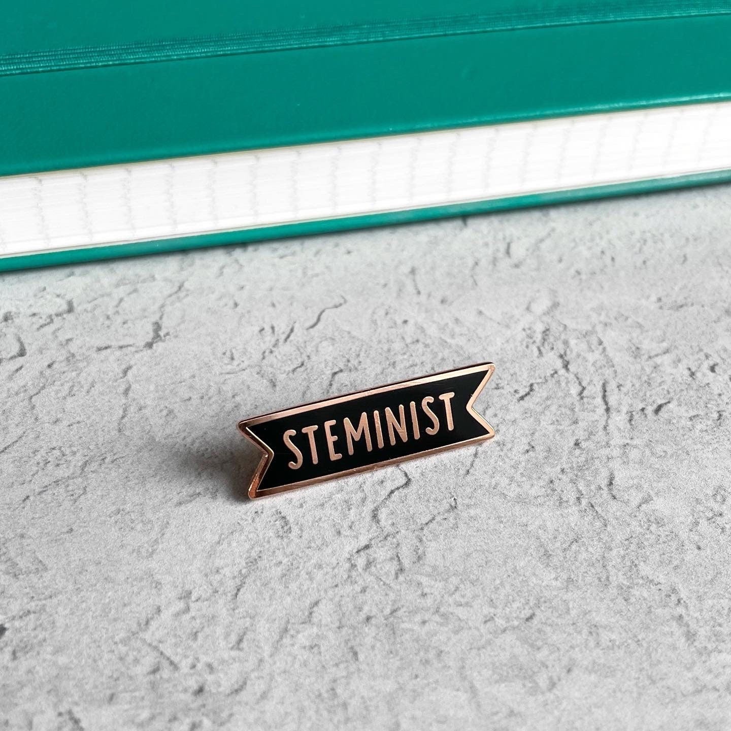 Enamel pin with 'STEMINIST' text on a textured surface