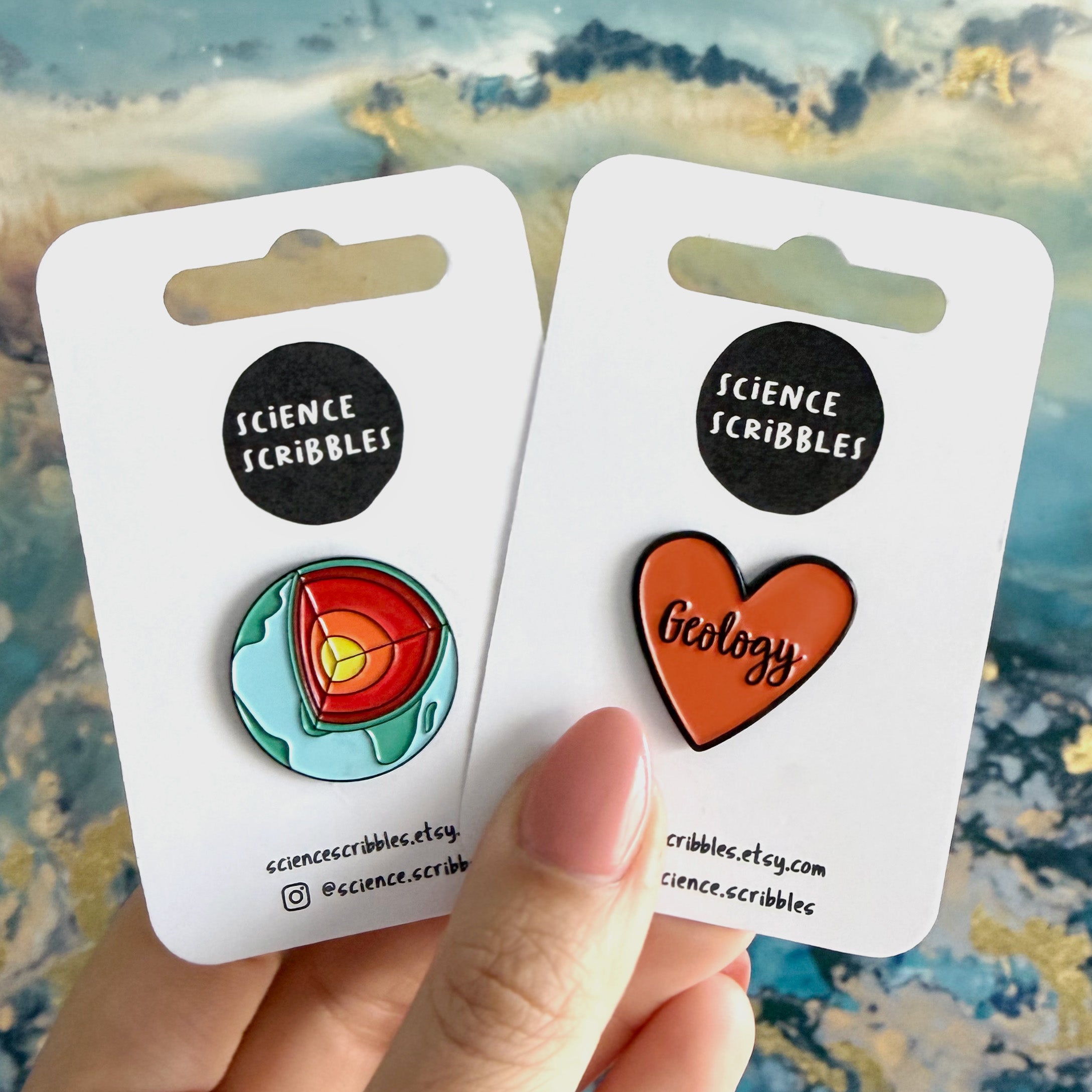 Two science-themed pins on cards held by a hand with a colorful background