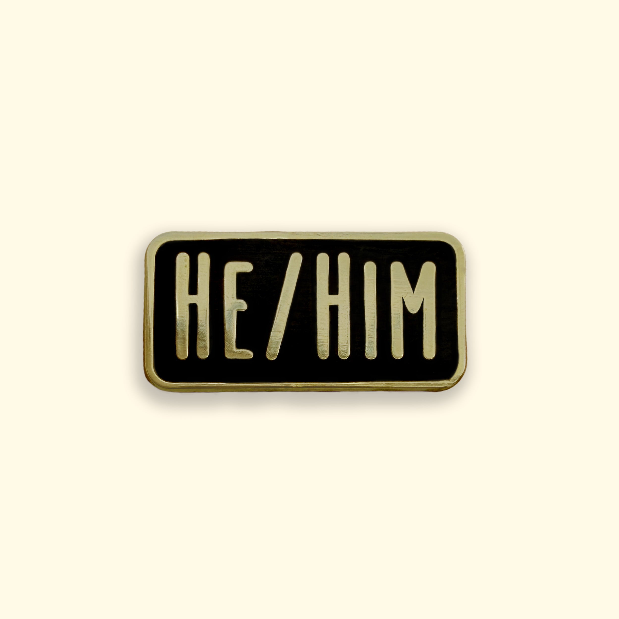 Enamel pin with 'HE/HIM' text on a beige background