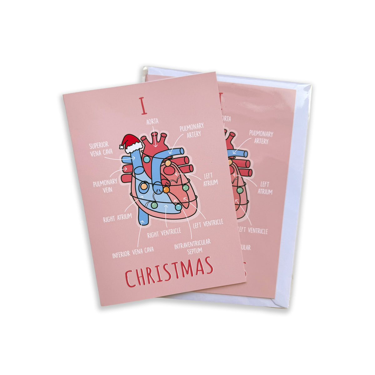 A pink Christmas greeting card with an anatomical heart illustration and the word 'CHRISTMAS' printed on it, shown on a pale pink background.