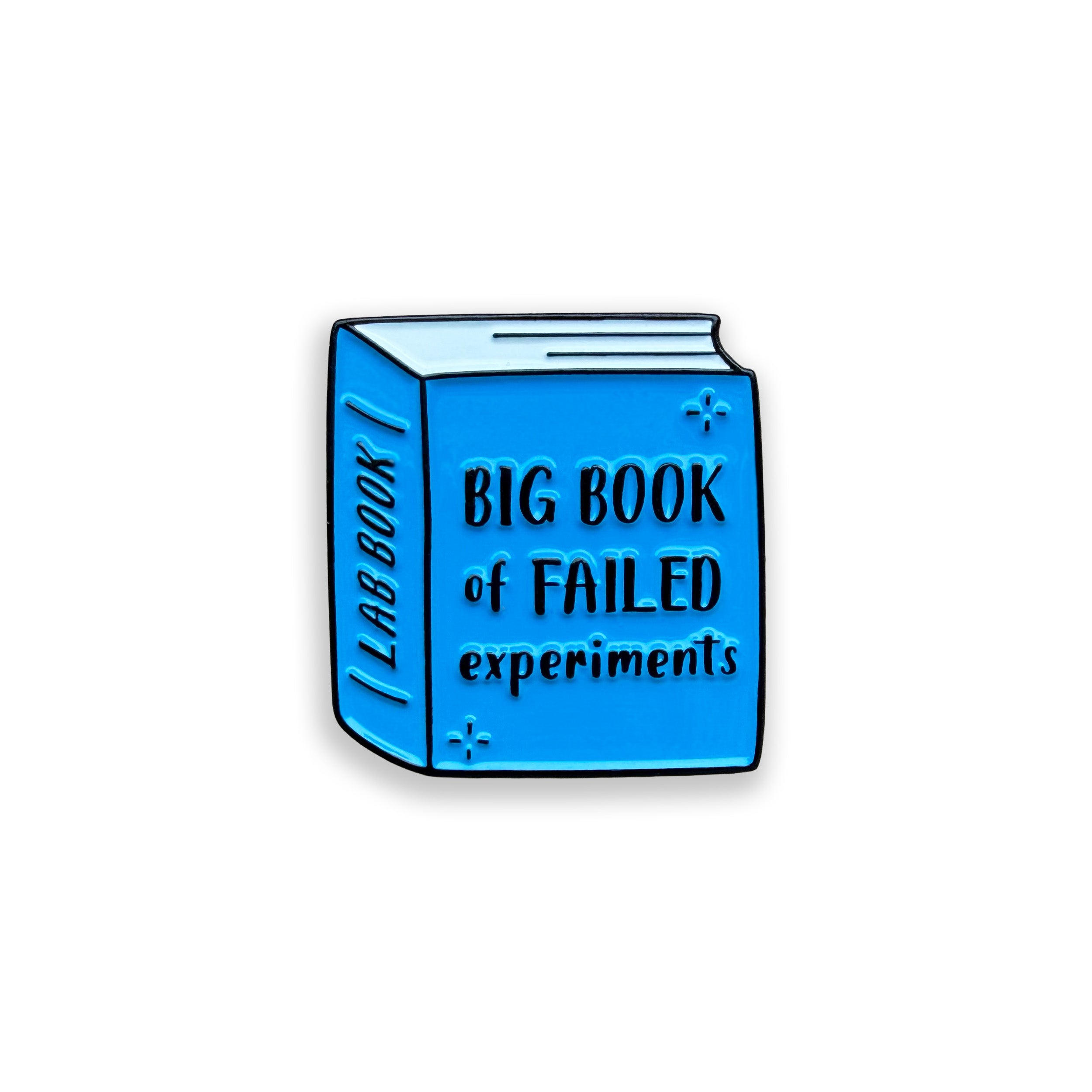 Blue enamel pin shaped like a lab book with 'Big Book of Failed Experiments' text on a white background