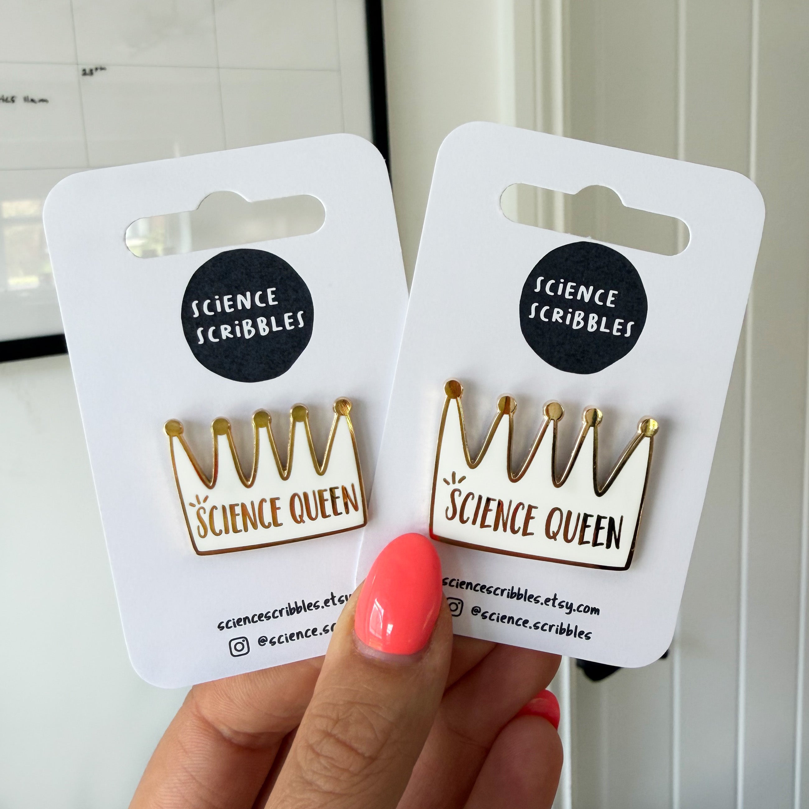 Two 'Science Queen' pins on cards held by a hand with pink nail polish.