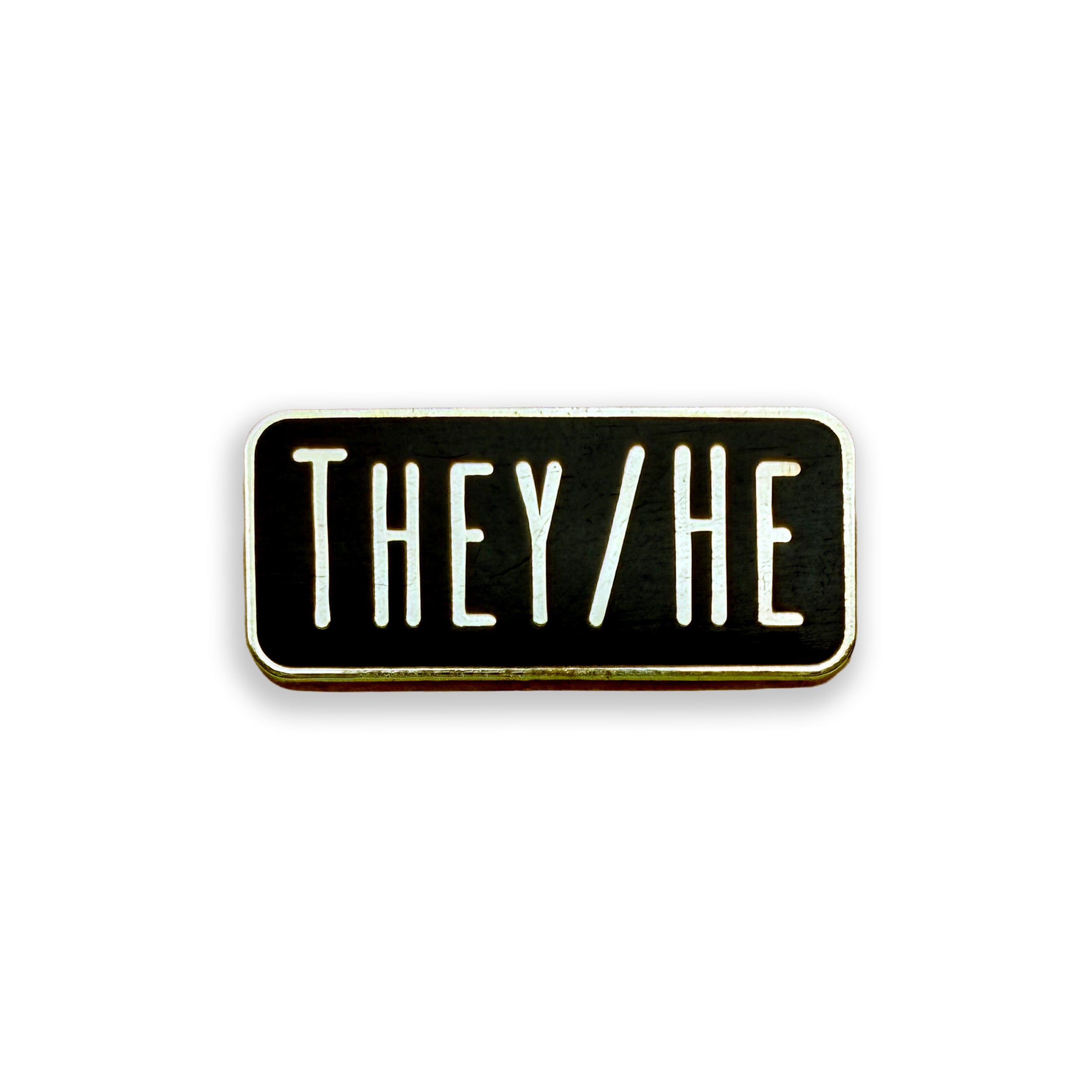 A rectangular enamel pin with a black face, white text reading 'THEY/HE', and a gold-toned metal border, shown on a plain white background.