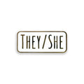 Enamel pin with 'THEY/SHE' text on a white background