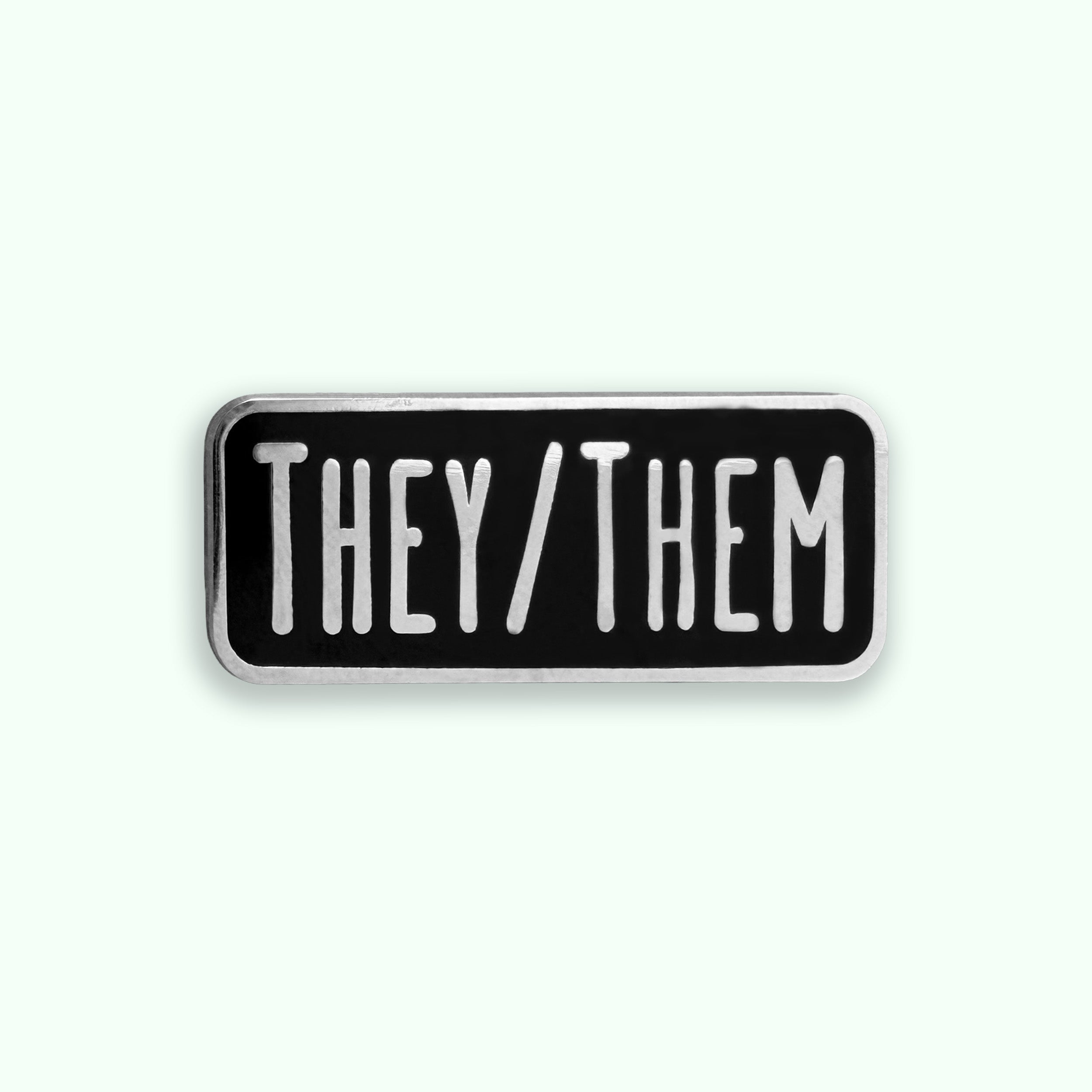 Black and white enamel pin with 'THEY/THEM' text on a white background